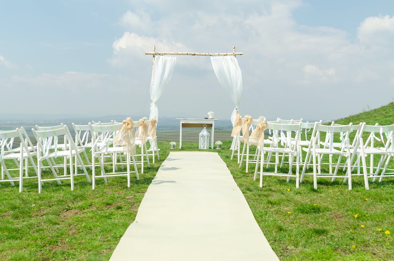 A wedding arch with flowers and chairs set up in a sunny field