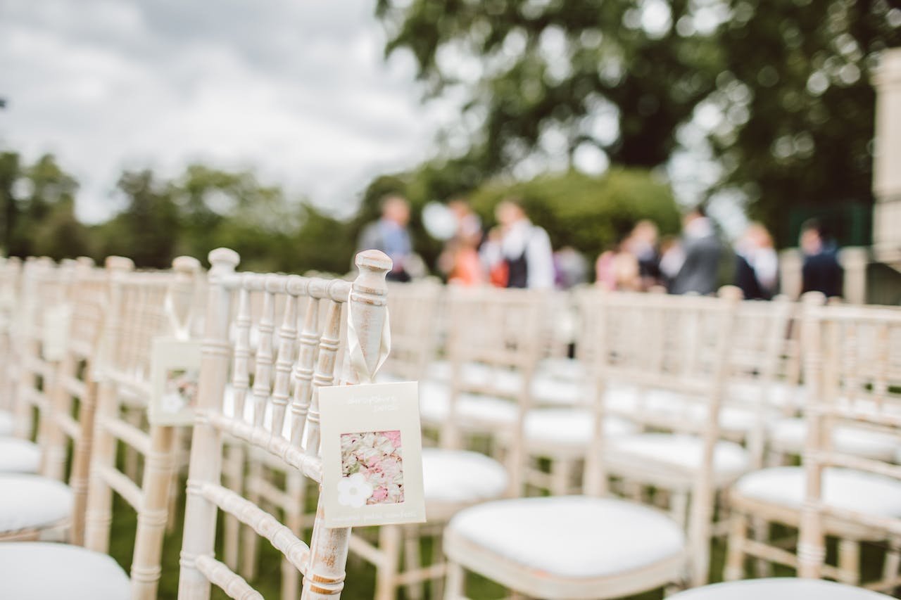 Rows of white wedding chairs outside with people in the background